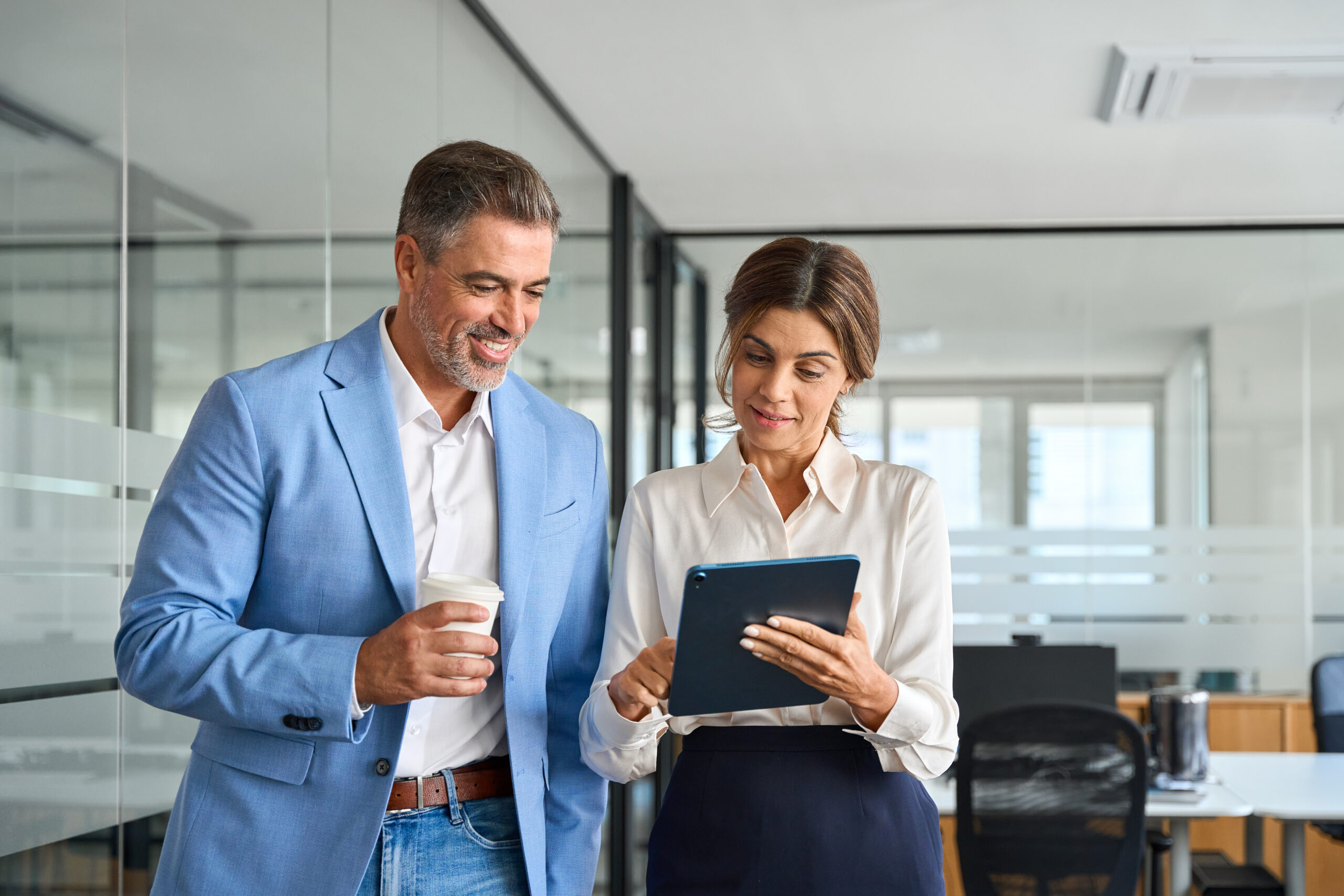 Team of two professional business people, business man and woman executives partners of middle age working together standing in office using digital tablet in corporate cooperation on project.