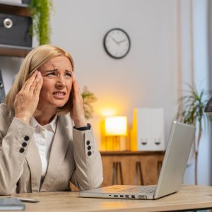 Tired mature businesswoman feeling headache working on laptop computer at home office desk, take back control of your business