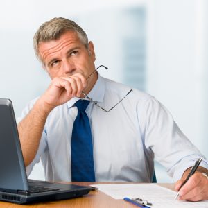Pensive mature businessman looking up with concentration and writing in his paperwork at office