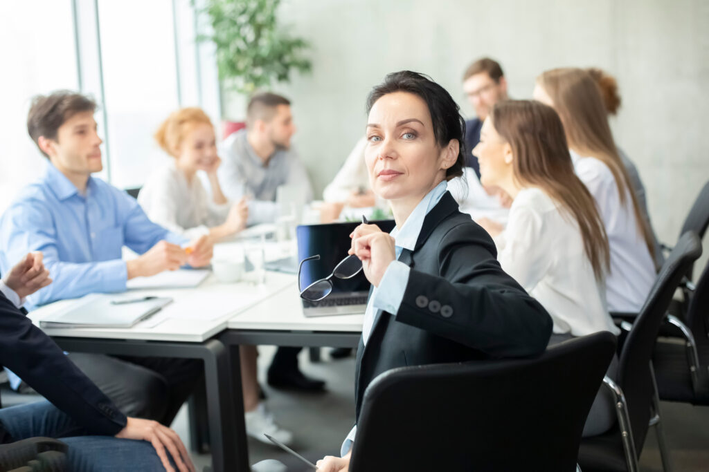 Confident Manager smiling to camera at meeting, colleagues working on background