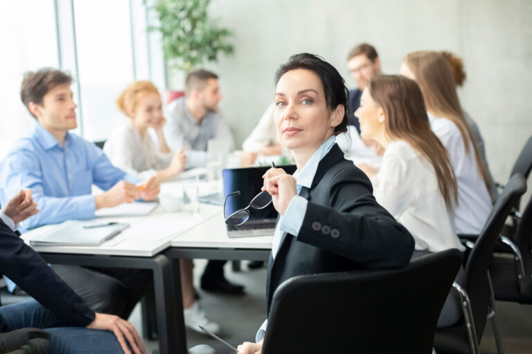 Confident Manager smiling to camera at meeting, colleagues working on background