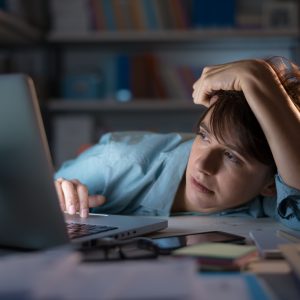 Sleepy exhausted employees working with her laptop, her eyes are closing and she is about to fall asleep, sleep deprivation and overtime working concept