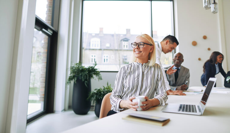 businesswoman drinking coffee and looking deep in thought while sitting at a boardroom table with colleagues in the background, dynamic scalable business