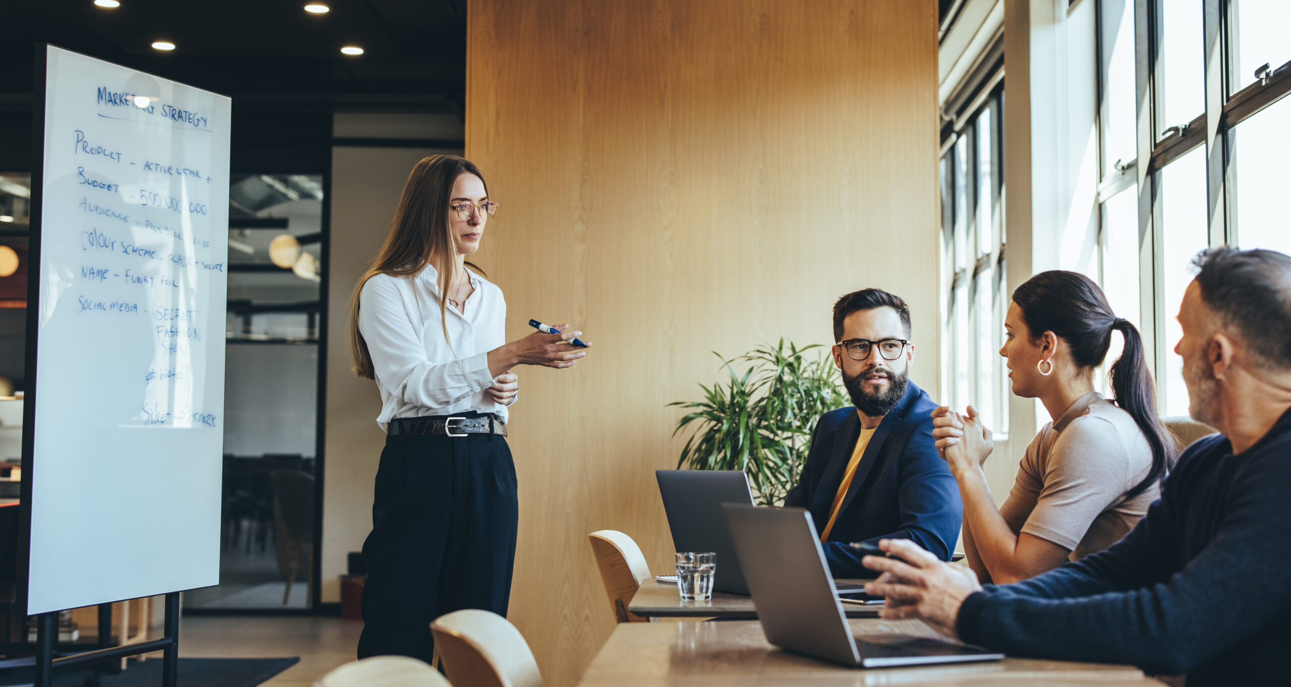 Businesswoman discussing her marketing strategy and ideas with her team, Female manager giving a presentation during a meeting with her colleagues in a modern workspace.
