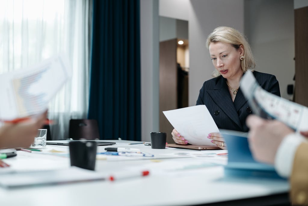 A focused businesswoman reviews paperwork during a professional meeting inside an office.