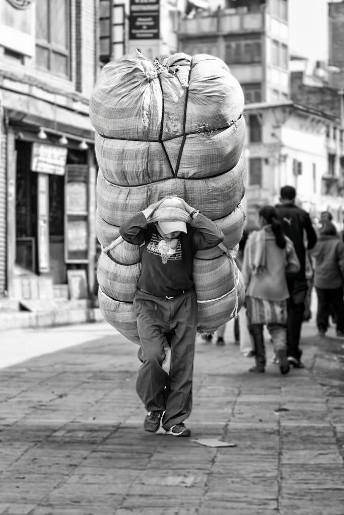 A man carries a massive bundle on city streets in Kathmandu, Nepal, showcasing daily life.