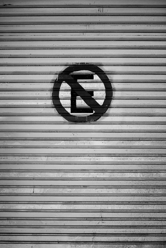 Black and white image featuring a no parking sign on a corrugated metal gate in Buenos Aires.