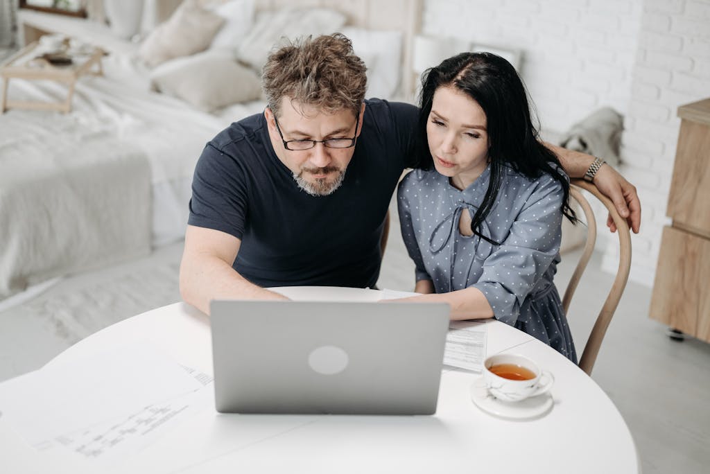 Couple working together on a laptop at home, discussing plans over tea.